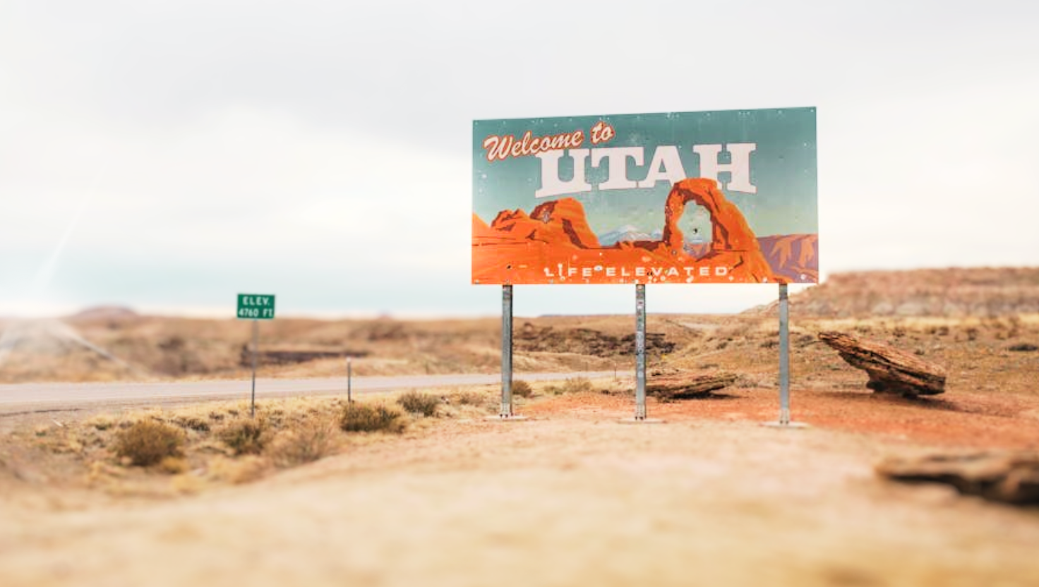 Welcome to Utah sign standing in a desert landscape near the Utah-Arizona border, with red rock formations and a cloudy sky